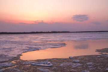 picturesque colorful ice drift on a calm wide river during the pink sunset with pink reflection on water