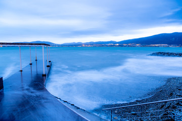 Gelendzhik beach in the evening in a storm. The waves at high speed turn into a blue fog. Pebble beach, breakwater. In the background, the Caucasus mountains, city of Gelendzhik