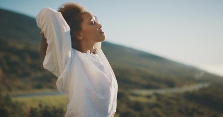 Young attractive african american woman raising her arms above her head and taking a relaxing deep breath outside, independent woman embracing life - Powered by Adobe