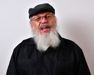 Old, overbearing jerk sneers into the camera. .. .Mature gentleman with a newsboy cap and black guayabera shirt and long white beard...