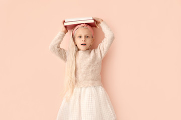 Surprised little girl with books on color background
