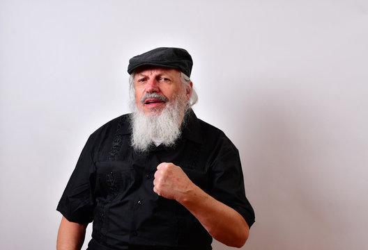 Old man makes a power gesture with his fist... .Mature gentleman with a newsboy cap and black guayabera shirt and long white beard..