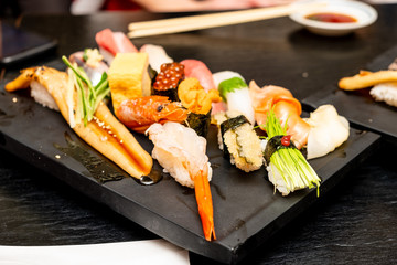 Real Japanese sushi in a restaurant in Tokyo. Set of sushi on a black plate made of stone.