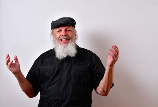 Old man making an explanation with both hands up... .Mature gentleman with a newsboy cap and black guayabera shirt and long white beard..