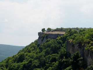 Mountain slope covered with dense green vegetation, table mountain with two standing cars, against the blue sky.