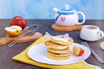 Dessert or snack, fried apples in the dough, sprinkled with powdered sugar, on a white plate on a dark concrete background. American cuisine. Selective focus.