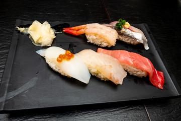 Real Japanese sushi in a restaurant in Tokyo. Set of sushi on a black plate made of stone.