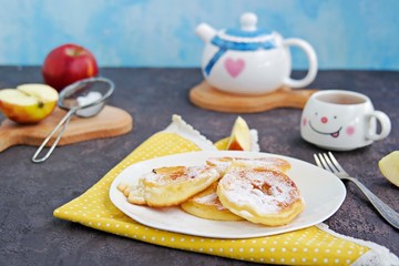 Dessert or snack, fried apples in the dough, sprinkled with powdered sugar, on a white plate on a dark concrete background. American cuisine. Selective focus.