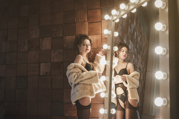 sexy girl in black lingerie and fur coat posing in front of the mirror