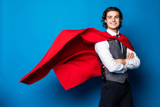 Young handsome businessman in red superhero cape over blue background