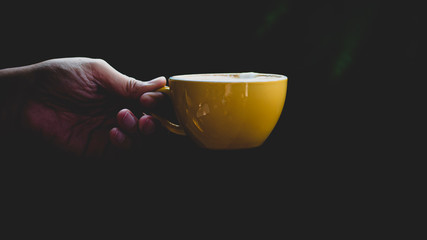 Close-up isolated hand holding yellow mug on black background. Hand hold simple yellow cup. Perfect for both tea and coffee.