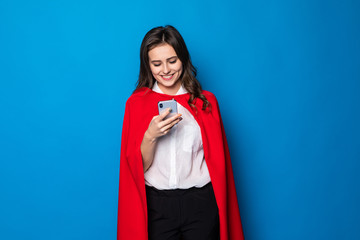 Business, power and people concept. Young smiling businesswoman in red superhero use on the phone on blue background