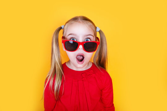 Shocked little girl in red sunglasses over yellow background