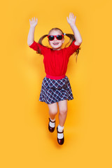 funny little girl in red sunglasses jumping on yellow background