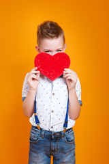 Close up ol funny little boy hiding her eyes behind red heart on yellow background