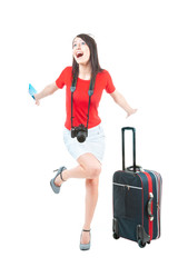 A beautiful young woman in a red blouse and white skirt, holding a blue ticket and with photo camera, is happy when her flight was announced, isolated on a white background.