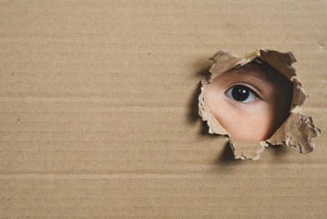 A child eye looking through a hole on a cardboard box. Conept of spy and stalker