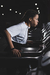 Fototapeta na wymiar Side view of african american woman puffing out cheeks while running on treadmill