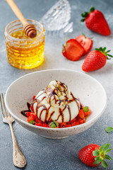 Gourmet burrata cheese with strawberry tartare with mint, honey and balsamic in a light plate on a gray concrete or stone background. Breakfast.  Mediterranean (Italian) cuisine. Selective focus