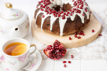 Chocolate muffin round hole (pie, cake, cake) with white icing and pomegranate on a white table. English dish for the holiday, English tea party