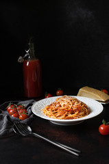 Pasta with tomato sauce and parmesan. White plate with spaghetti in tomato sauce on a dark background. Traditional Italian food.Low key, vertical, copy space