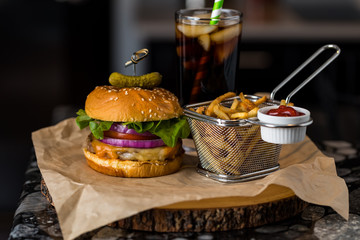 Front facing close up view of a burger and fries ready for eating with a soft drink in behind.