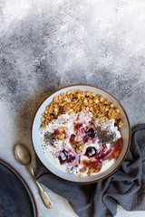 Granola with nuts, greek yogurt, organic jam and chia seeds served in a white bowl and a copper tray. Healthy breakfast, healthy eating concept. Gray background, top view, copy space