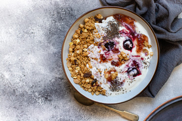 Granola with nuts, greek yogurt, organic jam and chia seeds served in a white bowl and a copper tray. Healthy breakfast, healthy eating concept. Gray background, top view, copy space