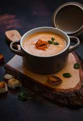 Cream sweet potato soup with sweet potato chips, breadcrumbs and herbs served in vintage copper plates on a vintage tray on a dark background. Vegetarian cream soup, healthy food. Close-up, copy space
