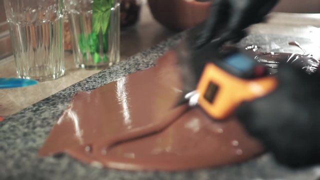 Confectioner Tempering Chocolate with thermometer and spatula on the marble sone