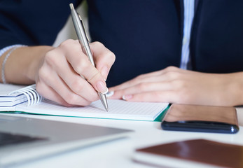 Young businesswoman writing in notepad while sitting at the office. Female hands holding a pen and making notes close up.