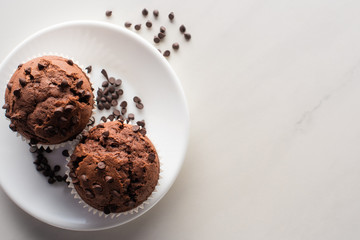 top view of fresh chocolate muffins on white plate on marble surface
