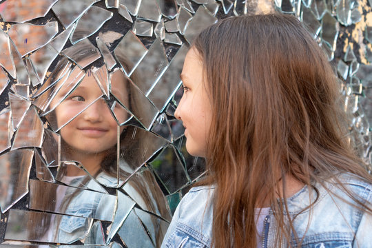 Young girl looks in a broken mirror and smiles on a mirror.