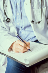 Female doctor hand hold silver pen filling patient history list at clipboard pad. Panacea and life...