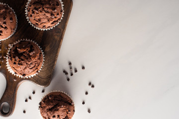 top view of fresh chocolate muffins on wooden cutting board on marble surface