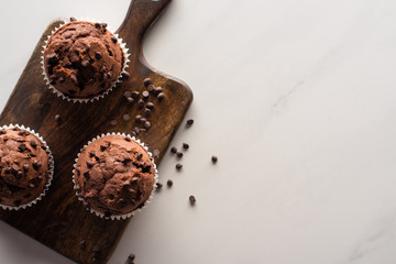 top view of fresh chocolate muffins on wooden cutting board on marble surface