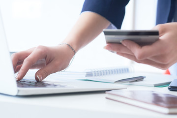 Businesswoman inputting her password and login to carry out online banking operation on laptop pc in the office. Woman's hand holding credit card close-up.