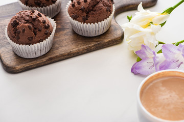 fresh chocolate muffins on wooden cutting board near flower and coffee