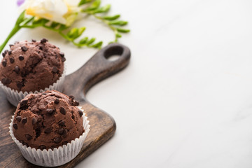fresh chocolate muffins on wooden cutting board near plant on marble surface