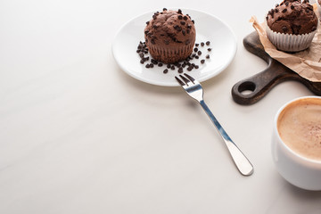 fresh chocolate muffins on wooden cutting board and plate with fork near coffee