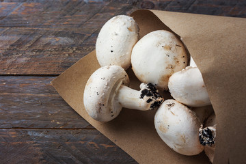 Bunch of freshly picked white button mushrooms in brown Kraft paper bag on rustic wood table. Plastic free shopping healthy vegan plant based diet concept