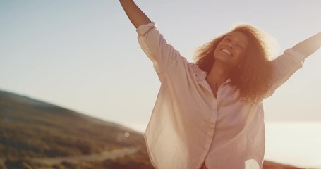 Happy carefree young african american woman smiling and raising her arms celebrating at sunset, joyful independent black woman achieving her dreams, flying into the sunset