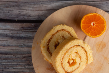 Orange roll cake and orange on wooden plate.