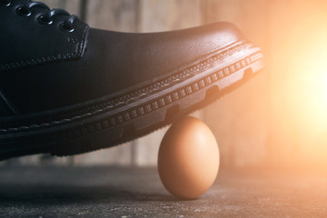 Black boot steps on a fragile chicken egg. Concept, weak defenseless, care and custody.