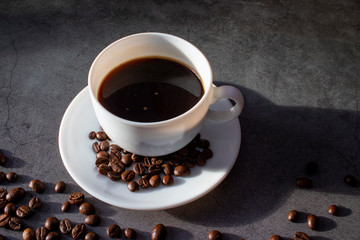 White cup with saucer and coffee beans, aromatic, hot coffee on a dark flat lay