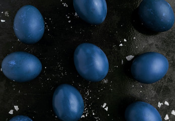 Easter eggs painted in classic blue monochrome style close up on a black surface with icing crumbs....