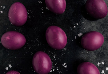 Easter eggs painted in purple monochrome style close up on a black surface with icing crumbs. Eggs...
