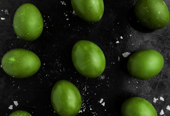 Easter eggs painted in green monochrome style close up on a black surface with icing crumbs. Eggs...