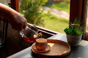 Young women hand pour hot tea in a cup on the wooden table.
