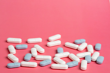 Scattered white and blue pills on a pink background